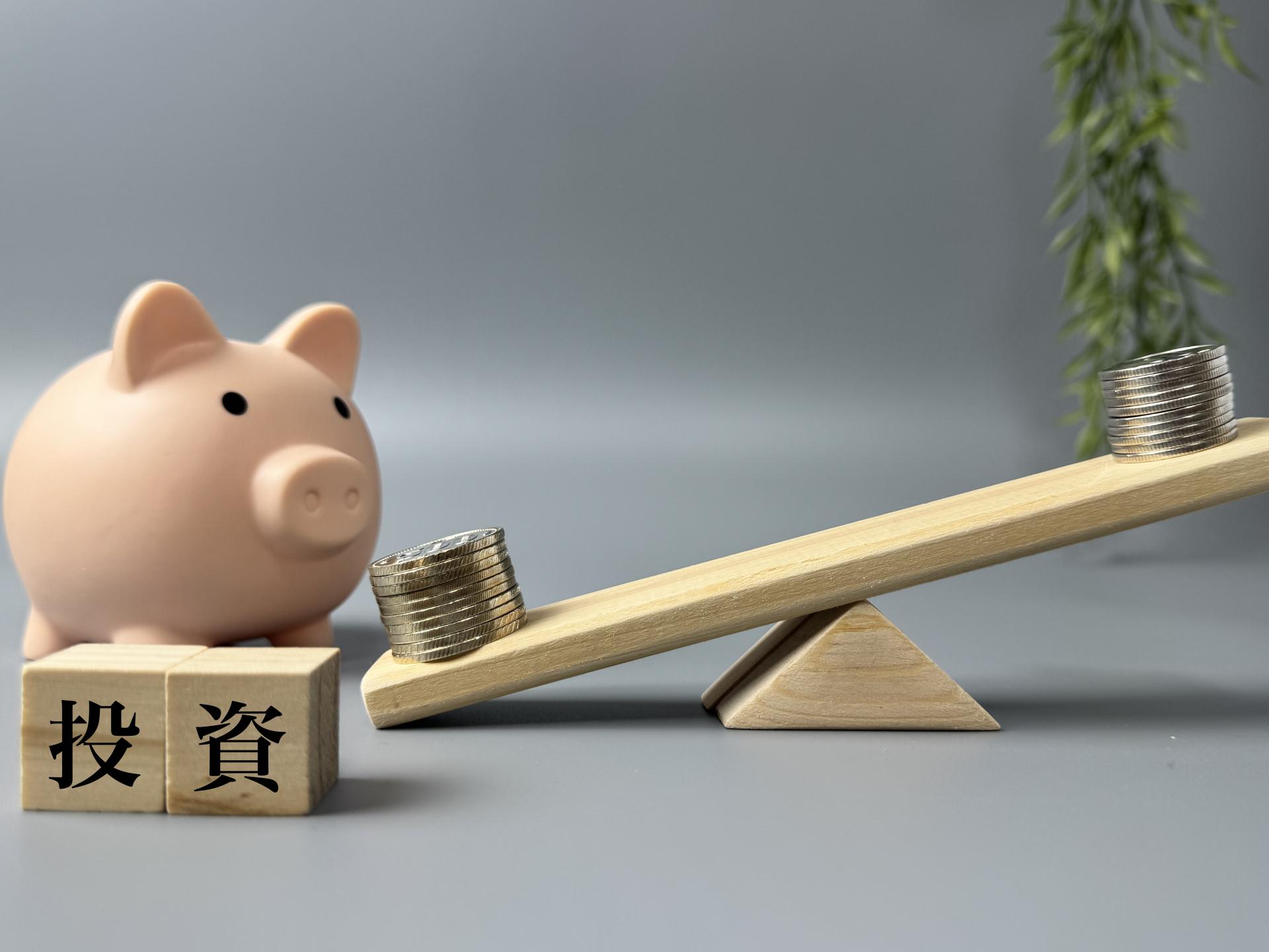 豚の貯金箱と投資の文字が乗ったシーソー